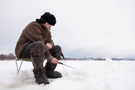Russian fisherman in earflapped fur hat and boots at winter fishingの写真素材