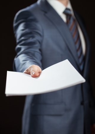 Businessman reaching out documents to you on black backgroundの写真素材