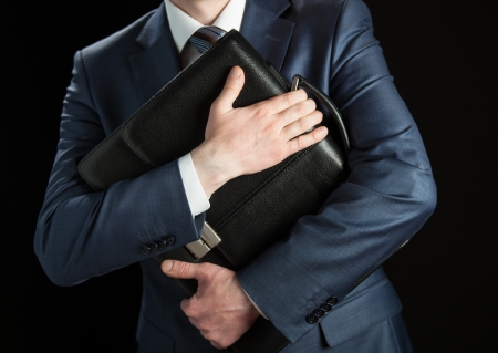 Businessman clasping briefcase to his breast on black backgroundの写真素材