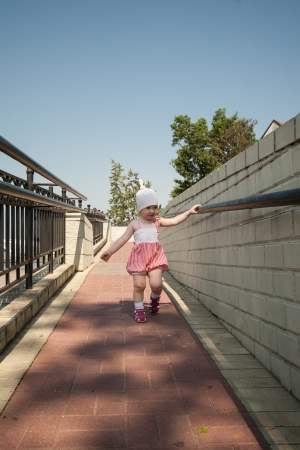 Baby girl walking along the path and holding the handrailの写真素材
