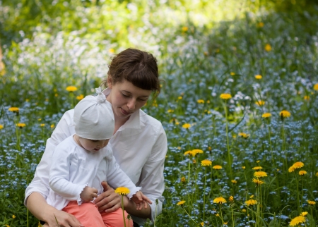 Little baby girl with her mother among foget-me-nots and dandelionsの写真素材