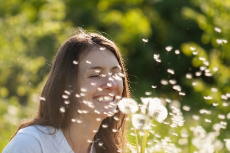 Happy young woman blowing at dandelions in sunny meadowの写真素材