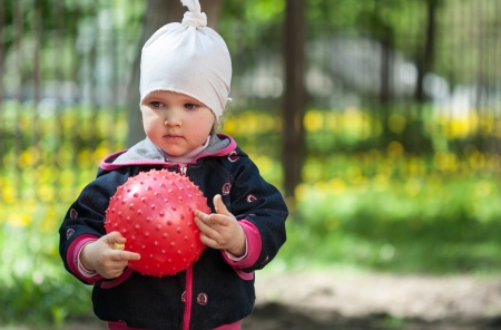 Pretty little girl playing with a red ball in a summer parkの写真素材
