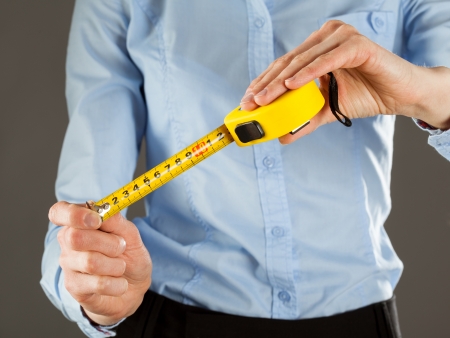 Unrecognizable young woman holding a tape measure, grey backgroundの写真素材