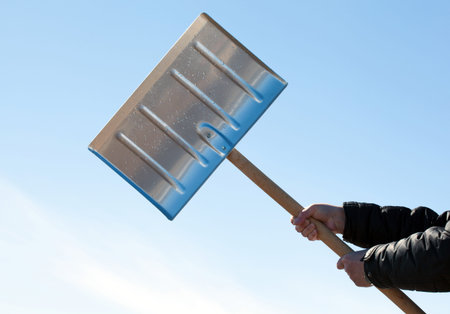 Hands holding shovel for snow removal on blue sky 
