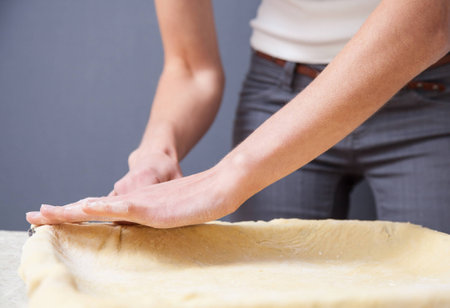 Woman's hands stretching dough on dark backgroundの写真素材