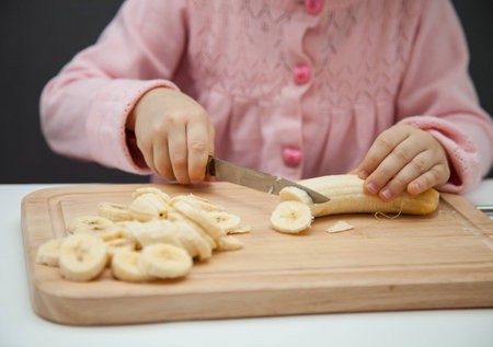 Little girl cutting a ripe banana on grey backgroundの写真素材