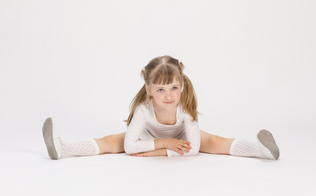 Pretty little girl sitting on the floor and doing exercise, white backgroundの写真素材