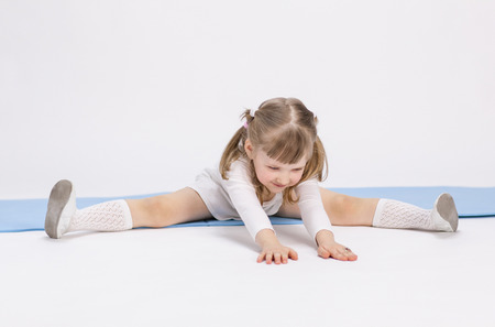 Pretty little girl sitting on the floor and doing exercise, white backgroundの写真素材