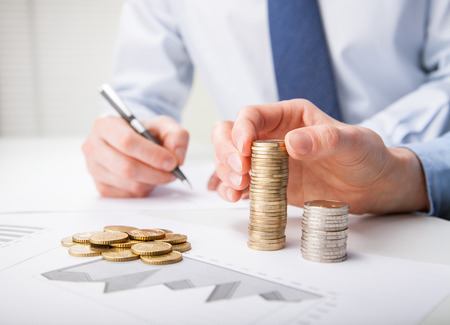 Business people calculating profit - closeup shot of hands counting coins and making notes on paperの写真素材
