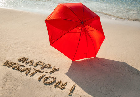 Beautiful seashore with umbrella and "Happy vacation" drawn on  sandの写真素材