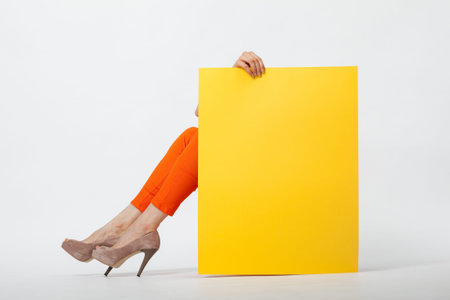 Unrecognizable young woman in orange pants holding blank yellow paper sitting on the floorの写真素材
