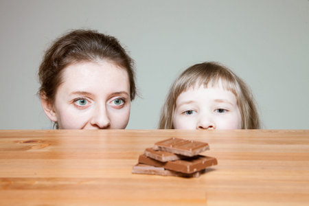 Young mother and her little daughter wanting to eat milk chocolate, neutral backgroundの写真素材