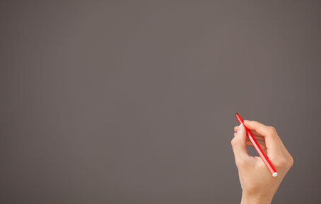 Female hand holding a red felt-tip pen on gray backgroundの写真素材