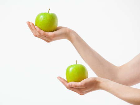 Female hands holding two green apples, white backgroundの写真素材