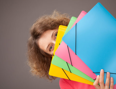 Young woman holding bright folders, gray background