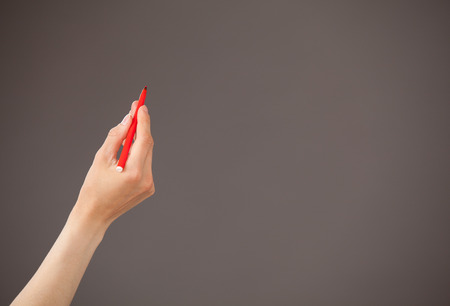 Female hand holding a red felt-tip pen on gray backgroundの写真素材