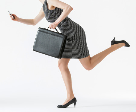 Unrecognizable businesswoman running and holding her cellphone and a briefcase, white backgroundの写真素材