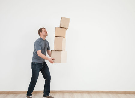 Smiling young man carrying many cardboard boxes, white background