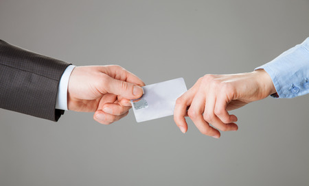 Business people passing a plastic card each other, grey backgroundの写真素材