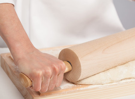 Unrecognizable cook's hands rolling out dough on wooden board, gray background