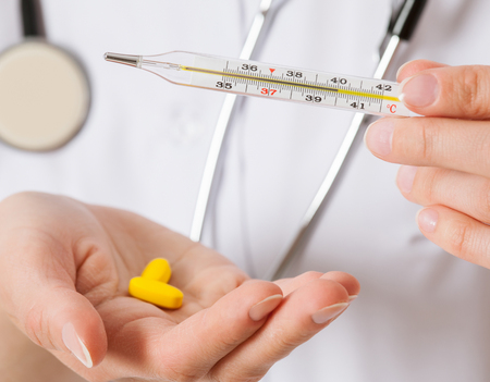 Doctor's hand holding thermometer and yellow tablets, closeup shotの写真素材