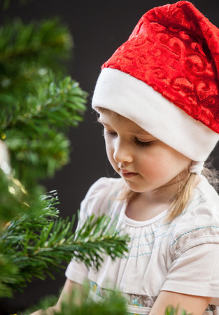 Beautiful little girl decorates the Christmas tree, dark backgroundの写真素材