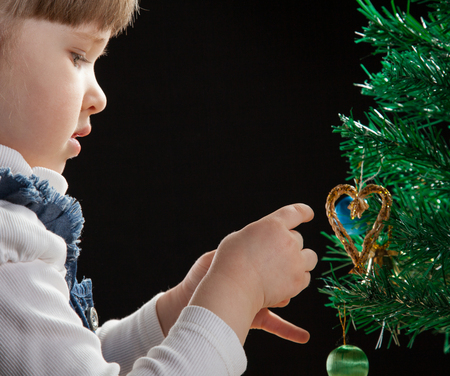 Beautiful little girl decorates the Christmas tree, black backgroundの写真素材