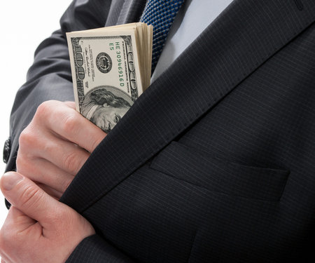 A businessman in a black suit putting money in his pocket isolated on white background
