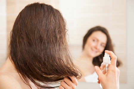 Smiling young woman applying hair spray in front of a mirror; haircare concept