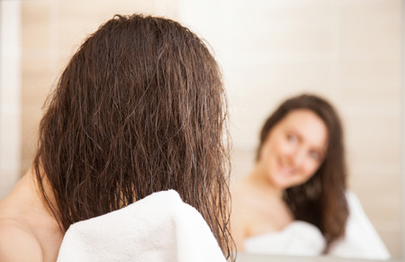 Smiling young woman wiping her hair after a shower in front of a mirrorの写真素材