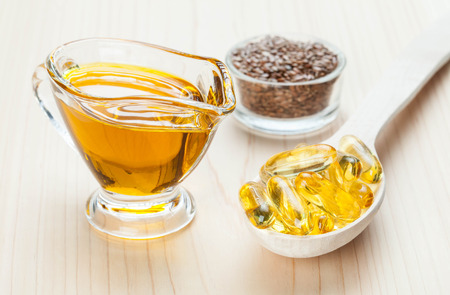 Small glass jug of flax oil, bowl with flax seeds and wooden spoon with fish oil capsules. Sources of Omega-3 for healthy hair, skin and nails.の写真素材