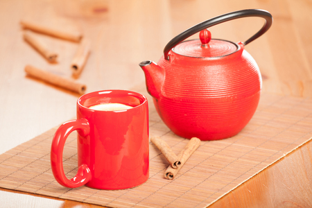 Morning tea set: red iron teapot, cup of tea and cinnamon on a bamboo matの写真素材