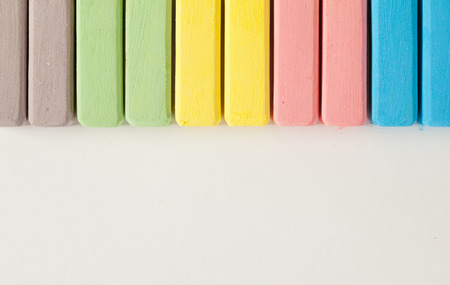 Multicolored school chalks lying in a row on white paper background with copyspace for your textの写真素材