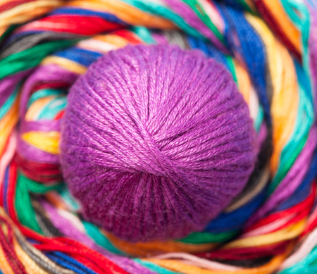 Purple clew of woolen thread lying on multicolored twisted threadsの写真素材
