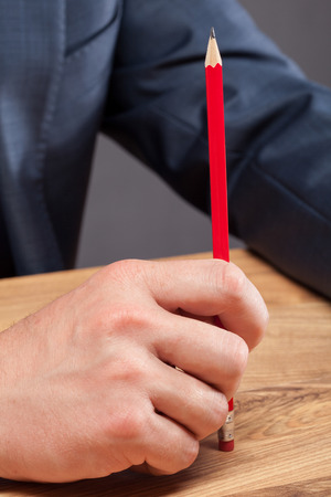 Businessman holding a red pencil and sitting at the table - closeup shotの写真素材