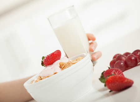 Healthy breakfast for healthy lifestyle! Unrecognizable person eating cornflakes with yoghurt and strawberry and drinking milkの写真素材