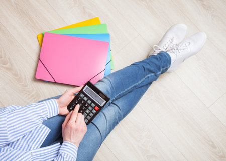 Unrecognizable woman using calculator sitting on the floor in a relaxed pose - upper viewpointの写真素材