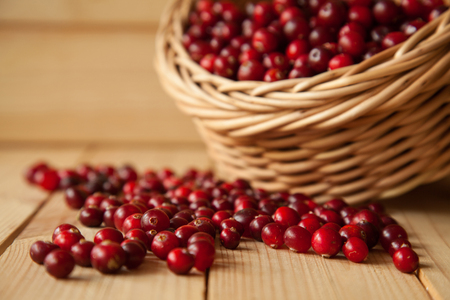 Cranberries scattering on wooden table and a straw basket in the backgroundの写真素材