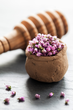 Composition of Calluna Vulgaris flowers in a small clay mug and wooden honey dipper on a slate backgroundの写真素材
