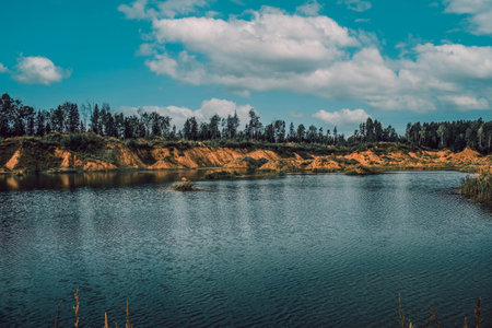 White clouds on a background of blue sky over a lake surrounded by treesの写真素材