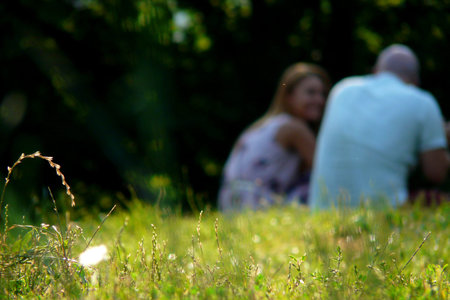 Couple sitting outdoors with back to camera. Relaxing on Green Grass.Park.の写真素材