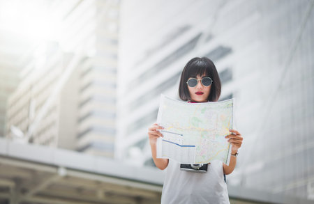 Hipster girl tourists searching for direction on the map the position while walking in the city,...