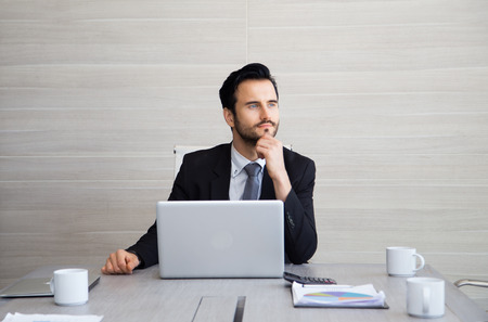 Young businessman thoughtful wearing suit holding hand on chin, looking out of modern office, planning future project, Business Concept.の写真素材