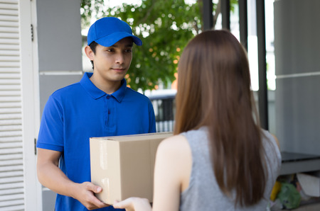 Handsome Young  man delivery person in blue uniform holding cardboard box send to customer,Delivery concept, Service concept.の写真素材