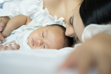Portrait of a beautiful young mother and baby sleep in a white bedroom. Parent and little kid...