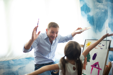 Happy Father's day.Funny portrait of smiling father and her daughter painting with watercolor on Easel happily at her home.の写真素材