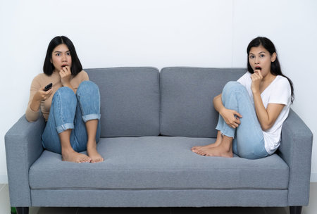 Two women sitting on the livingroom watching horror movie  looking at terrible plot feeling fearful...