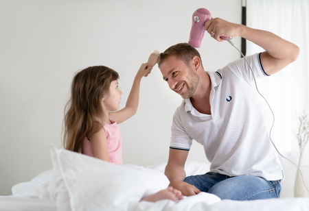 Cute litter girl take care of her handsome father.Father dries hair with a blow-dryer and little girl help comb to her father. Happy Father's day.の写真素材