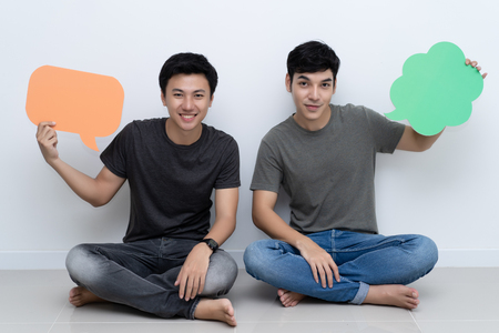 Two young Asian man holding copyspace placard sitting at homeの写真素材
